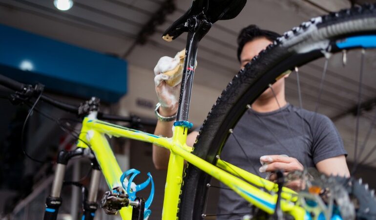 Oseba temeljito čisti kolo na stojalu, kar je prvi korak priprave kolesa na zimsko shranjevanje.
