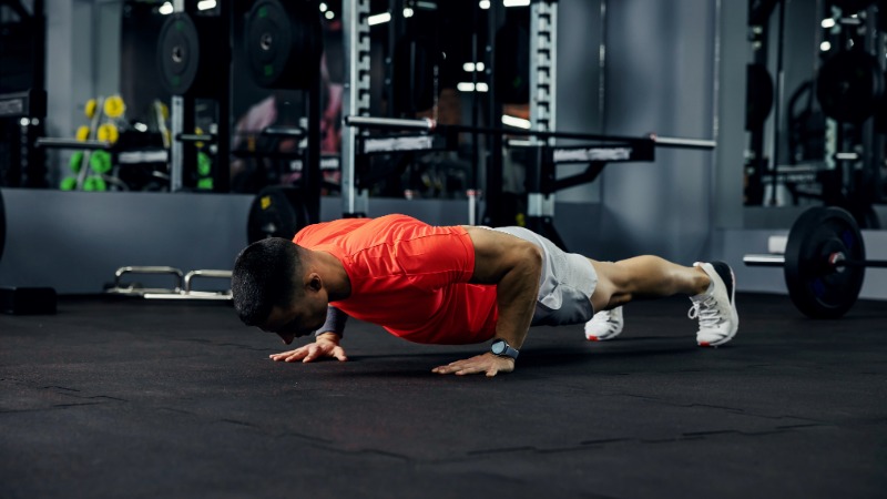 Moški v rdeči majici izvaja skleco s pravilno tehniko na fitnes podlogi.