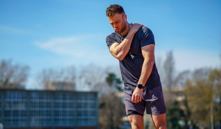 Rekreativni športnik se med aktivnostjo drži za ramo zaradi bolečine, kar ponazarja pogoste težave z ramenskim sklepom.