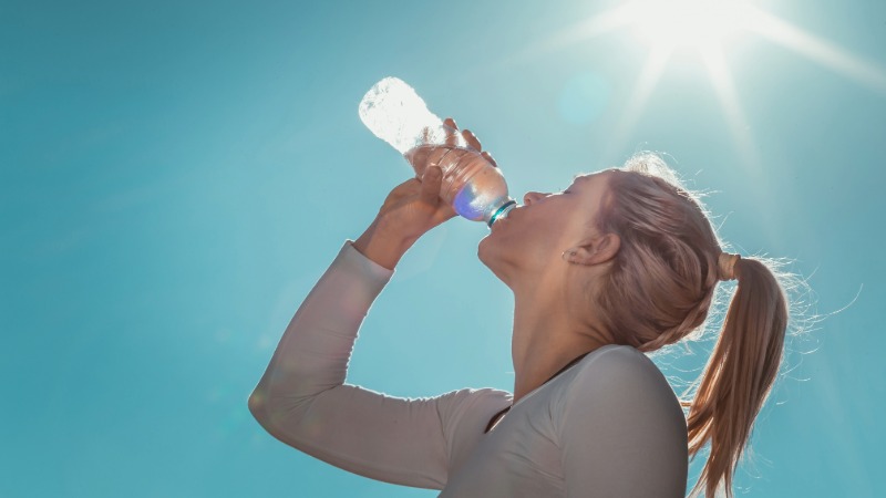 Rekreativec med aktivnostjo v naravi pije vodo iz steklenice za hidracijo.