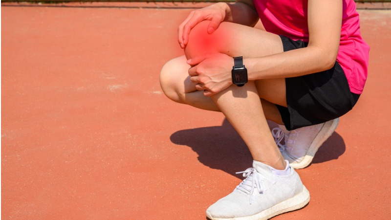 Tekačica se drži za zunanjo stran kolena, poudarjeno z rdečo barvo, kar prikazuje bolečino ob iliotibialnem traku (ITB sindrom).