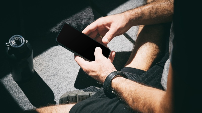 Oseba med vadbo brska po pametnem telefonu, s čimer ponazarja motnje in pomanjkanje osredotočenosti med treningom.