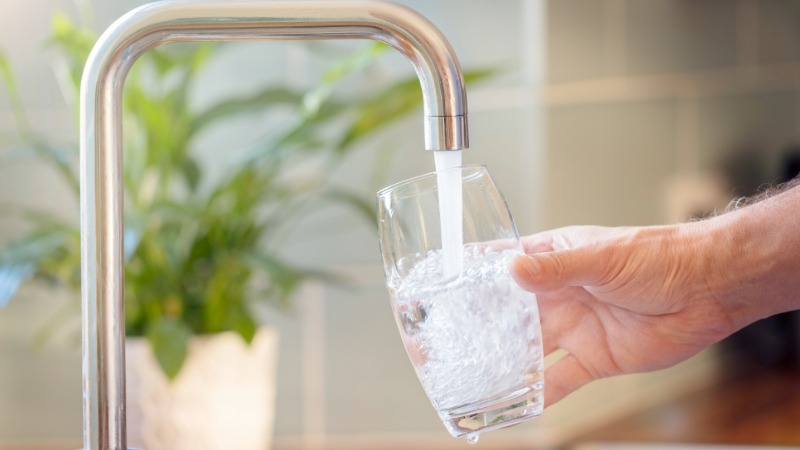 Oseba si toči kozarec vode iz pipe, kar ponazarja pomembnost hidracije za ohranjanje zdrave variabilnosti srčnega utripa (HRV).