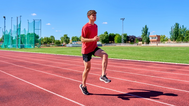 Mlad atlet na atletski stezi izvaja vajo visoki skiping kot del ogrevanja za izboljšanje tekaške kadence.