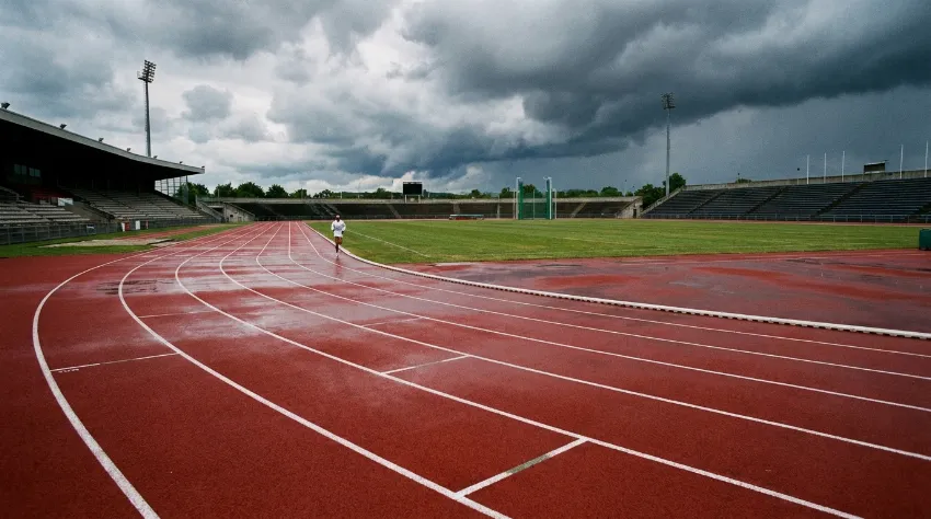 Prazna atletska steza z rdečo podlago in belimi črtami, idealna za Cooperjev test.