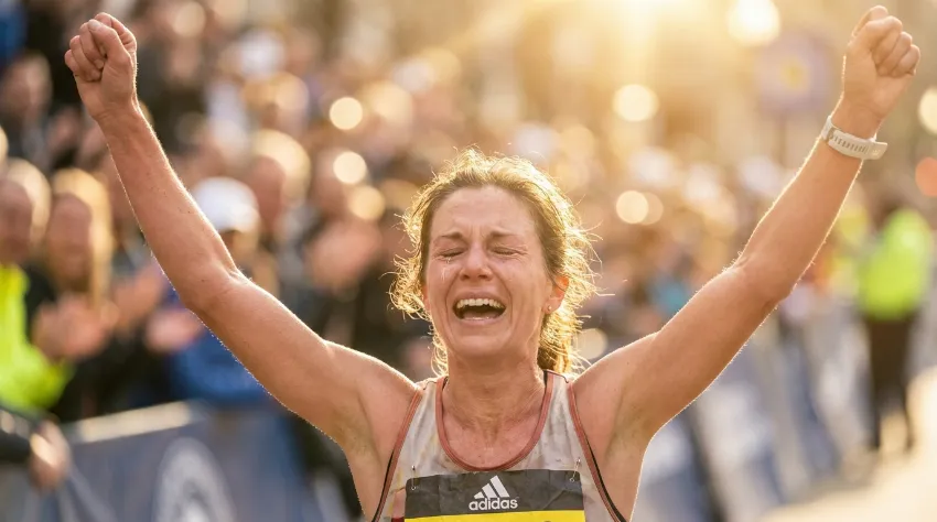 Srečna tekačica z dvignjenimi rokami v cilju maratona.