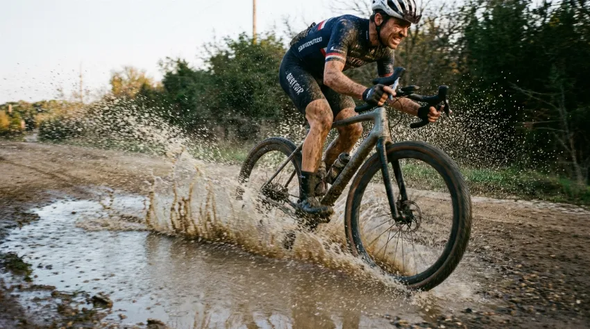 Gravel kolesar vozi skozi lužo na makadamski poti