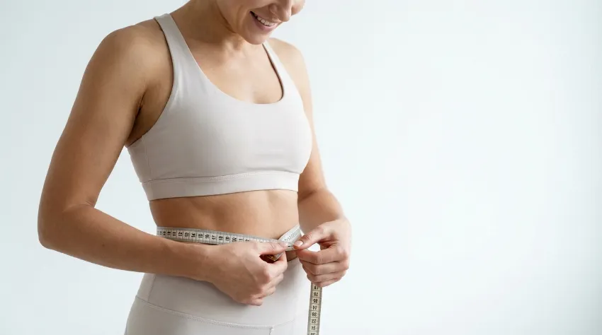Fit ženska si z merilnim trakom meri obseg pasu