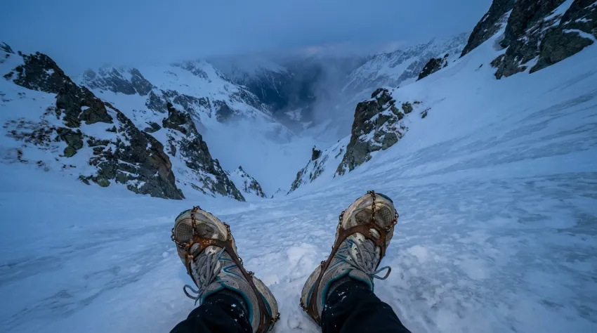Pogled navzdol po strmem poledenelem pobočju, ki prikazuje nevarnost uporabe neustreznih derezic.