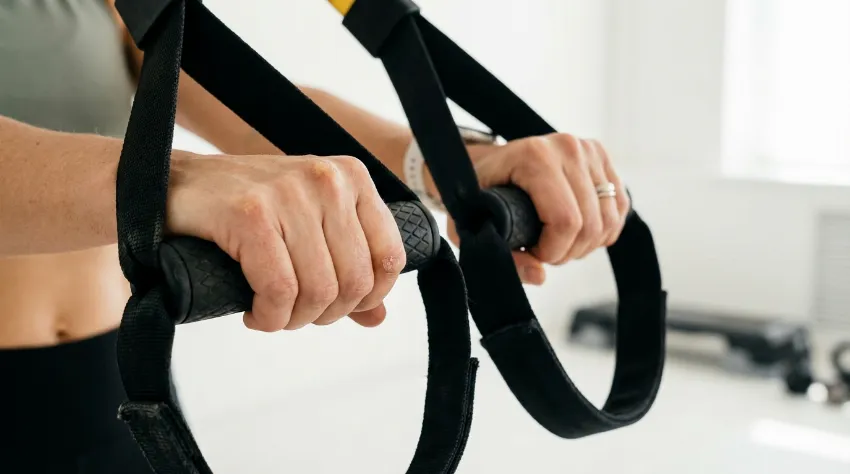 Detajl ročajev na TRX trakovih v rokah ženske