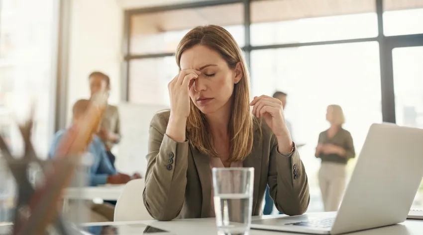 Utrujena ženska v pisarni se drži za glavo