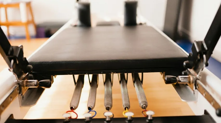 Bližnji posnetek kovinskih vzmeti in barvnih pritrditvenih točk na lesenem pilates reformerju, ki zagotavljajo edinstven, progresivni upor med vadbo.