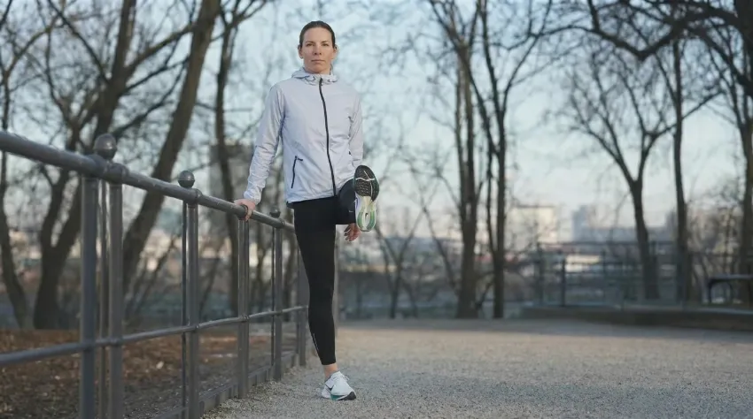 Tekačica se drži za ograjo in izvaja dinamične zamahe z nogo za ogrevanje kolkov.