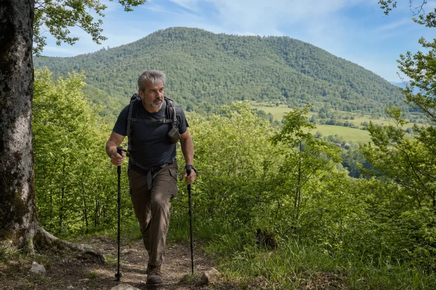 Pohodnik s treking palicami med dinamično hojo po gozdni poti proti Grmadi.