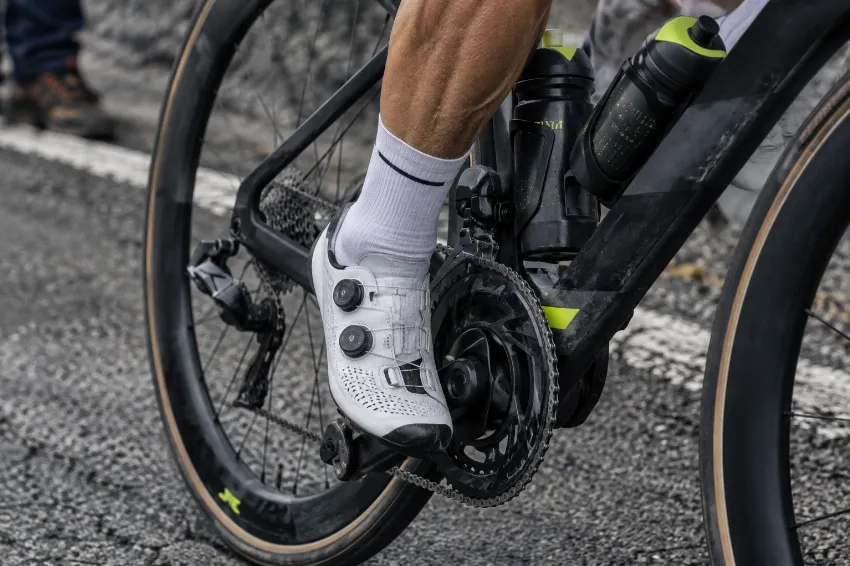Bližnji posnetek napete mišice in karbonskega kolesa med močnim pritiskanjem na pedala na strmem klancu.